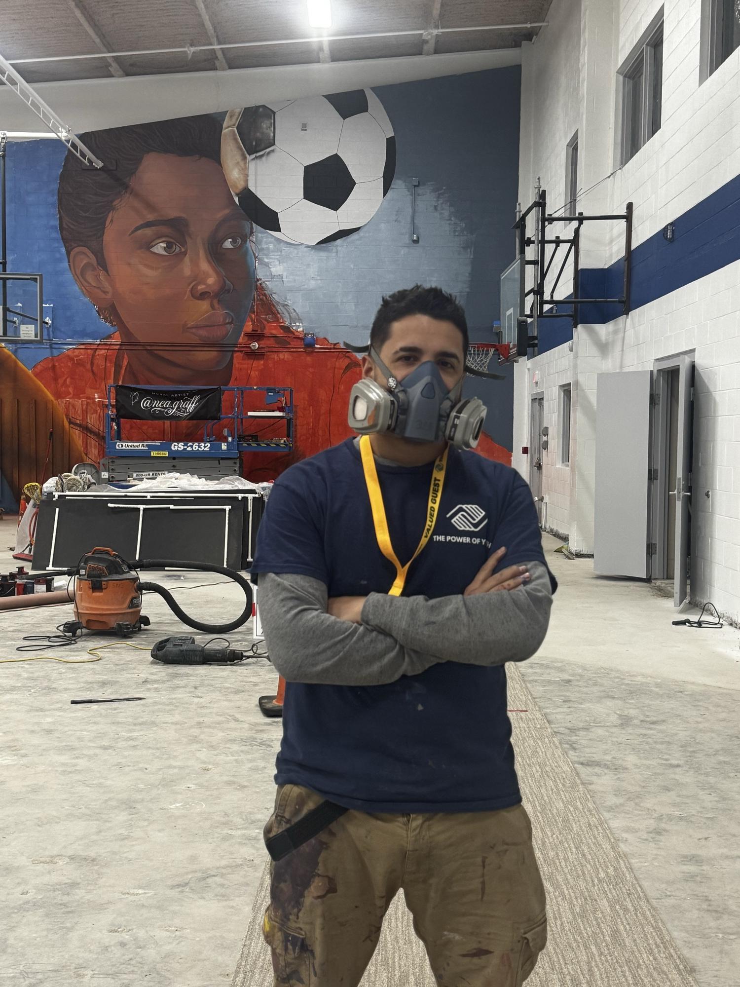 The artist in a respirator mask in front of a soccer mural