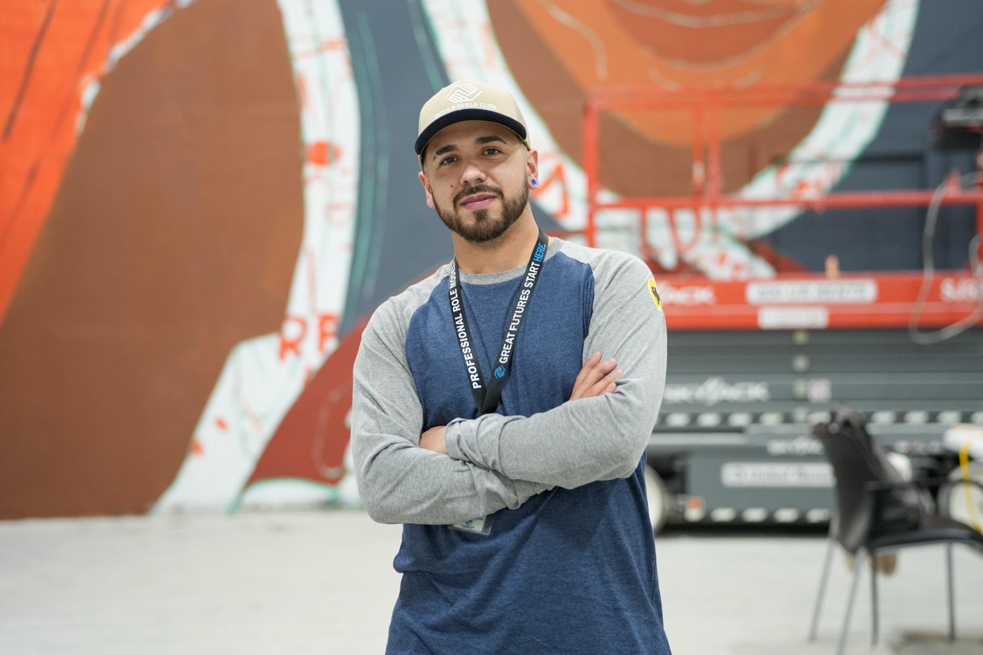 Cristhian Londoño, arms crossed, in front of a mural in progress