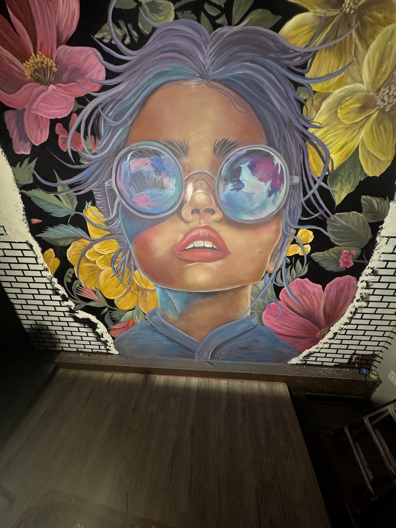 Mural of a girl in mirrored glasses surrounded by pink and yellow flowers