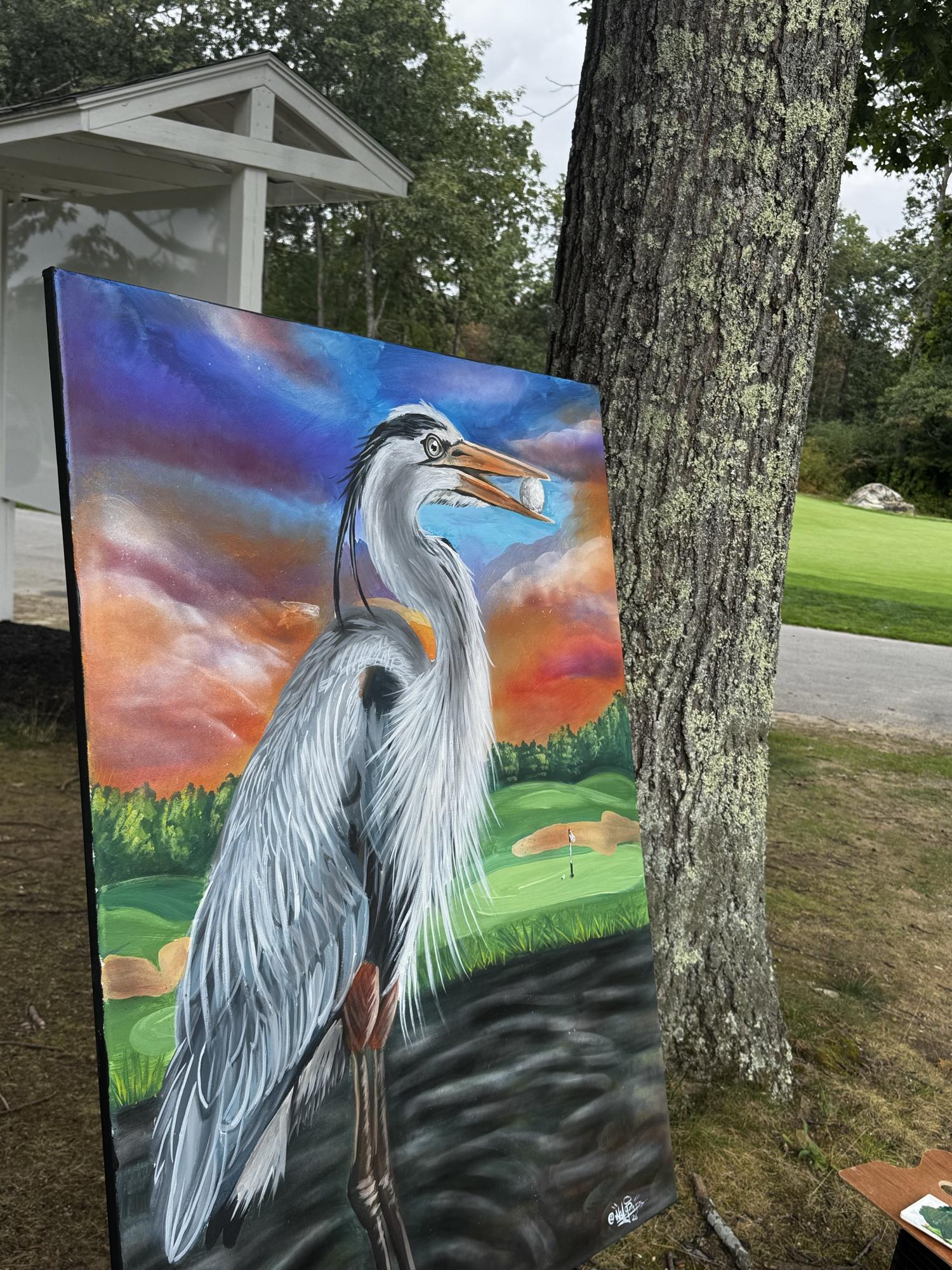 Live-painted canvas of a great blue heron at sunset, displayed outdoors