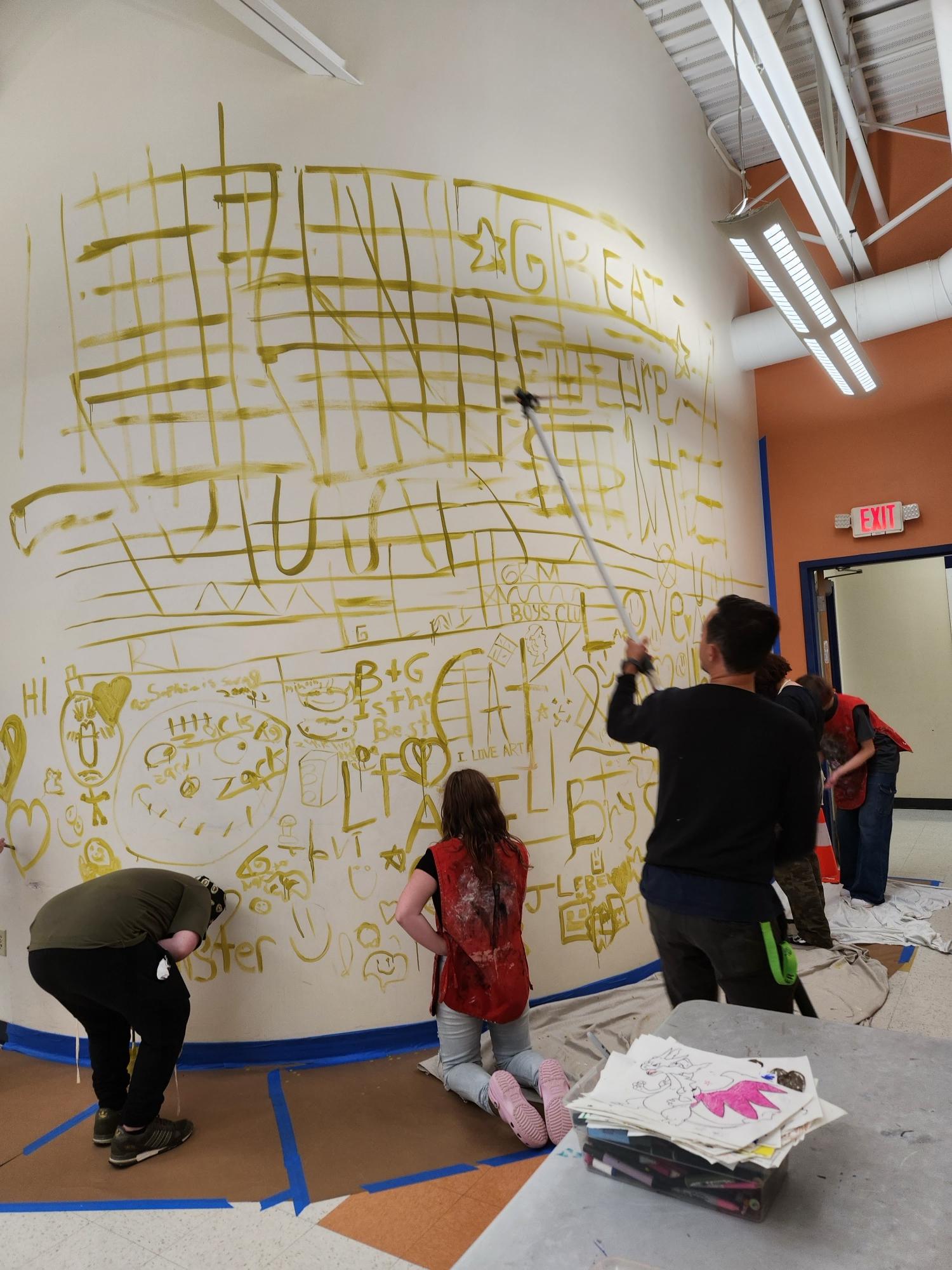 Children painting gold outlines on a white wall