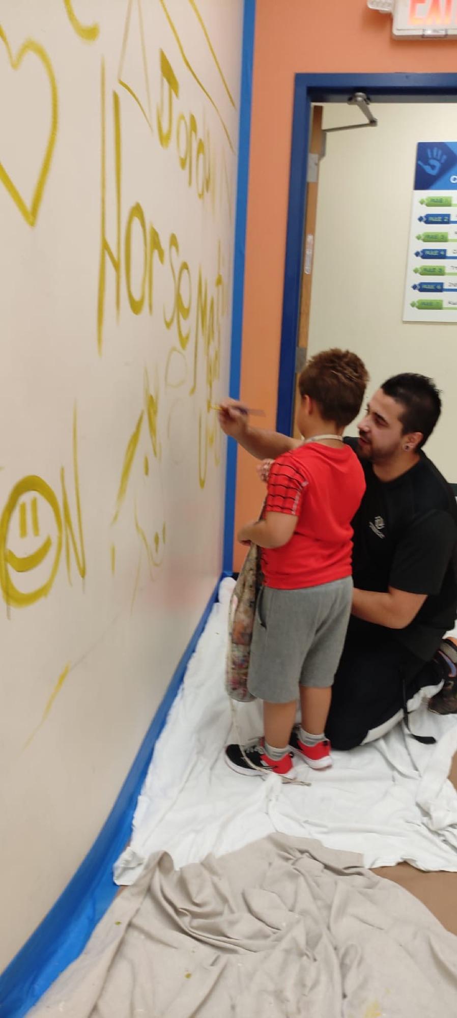 A child painting on a ladder-free low section of a mural