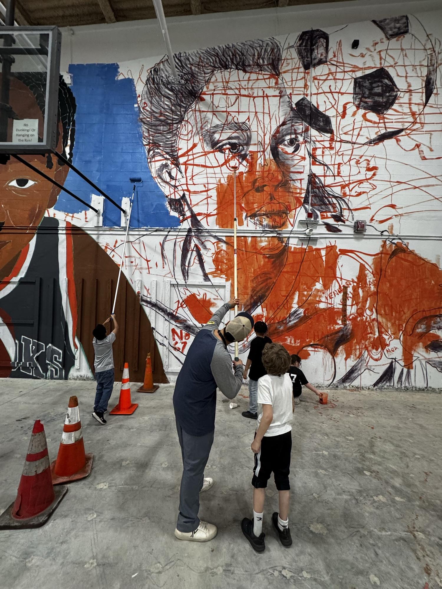 Kids and adults painting a large wall together in a gym